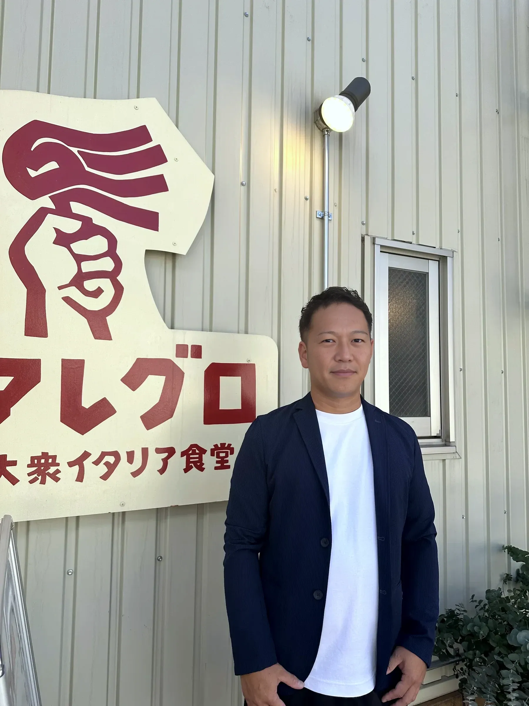株式会社レストランバンク 取締役 森本悠様、店舗看板の前に立つ